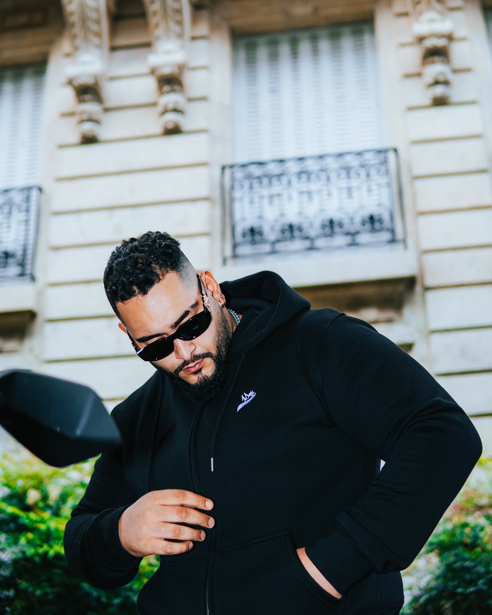 Photo d'un homme posant dans une rue de Paris portant un hoodie à capuche noir brodé ADMS SHOP