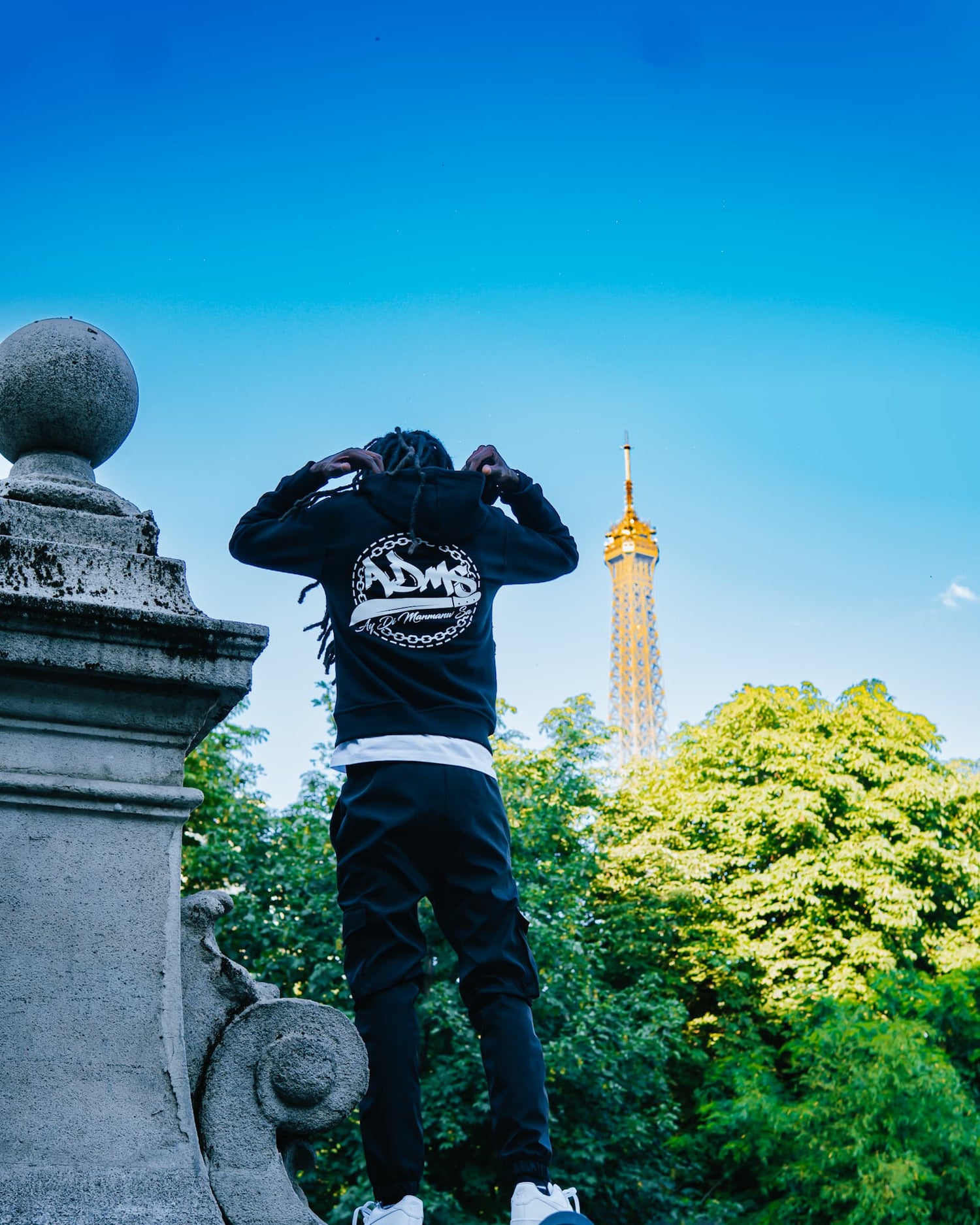 Photo d'un homme posant devant la Tour Eiffel à Paris portant un hoodie à capuche noir ADMS SHOP