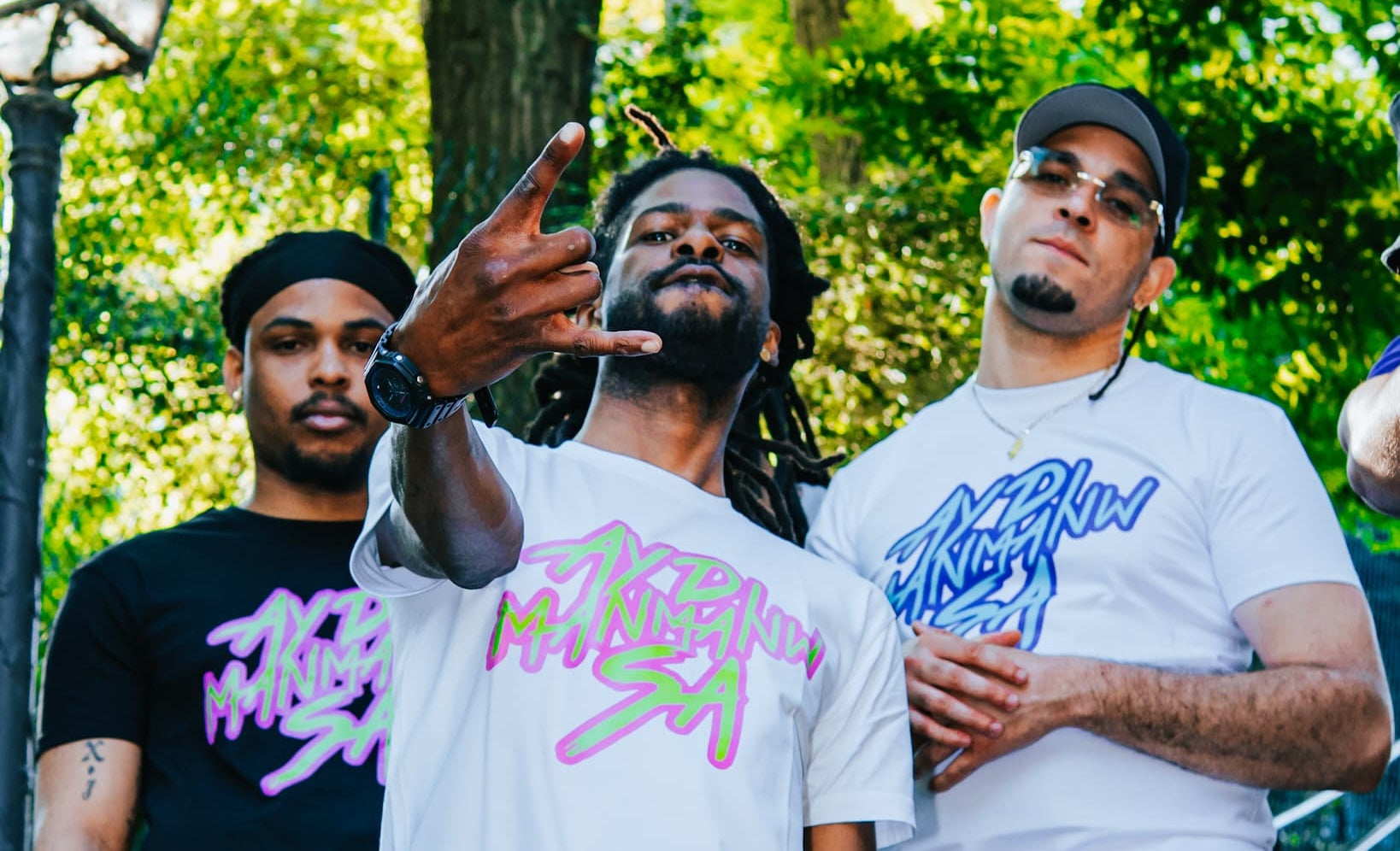 Photo de trois hommes posant à Paris portant des t-shirts ADMS SHOP avec la phrase Ayd Manmanw Sa en rose et vert ou bleu