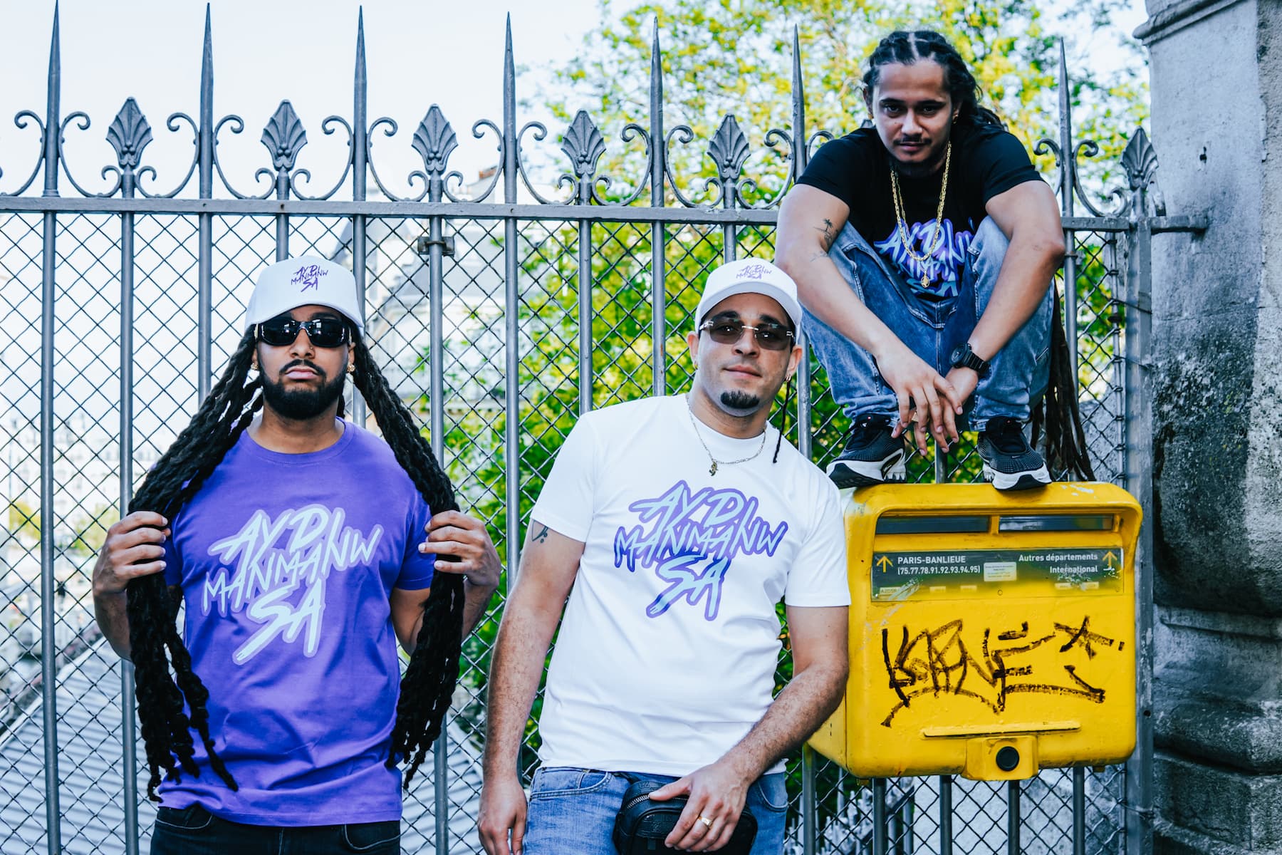 Photo de trois hommes à une station de métro de Paris portant des t-shirts ADMS SHOP avec la phrase Ayd Manmanw Sa en violet et bleu