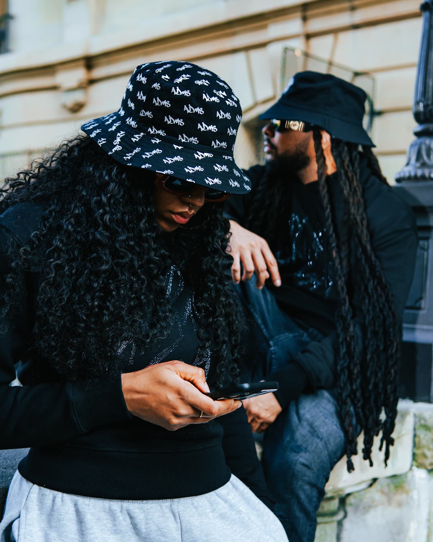 Photo d'une femme et d'un homme posant à Paris portant des t-shirts manche longue ADMS SHOP pailletés et des bob avec le motif ADMS